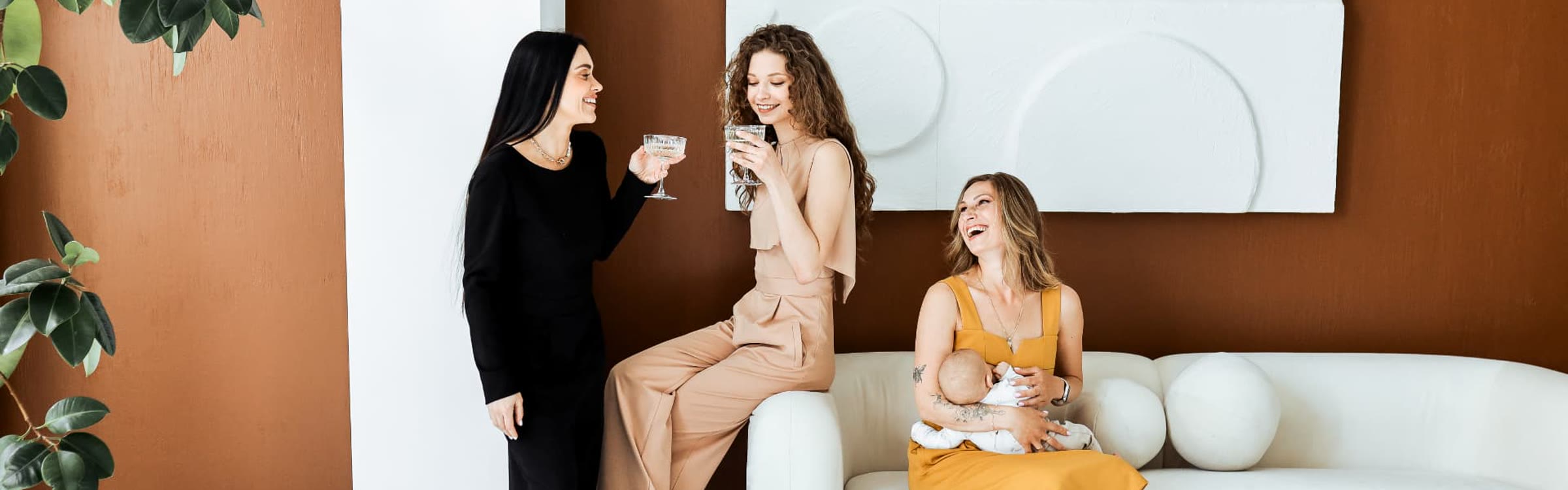 Three friends laughing together, one nursing her baby in a mustard nursing dress