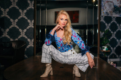 beautiful blond lady in a colorful baby blue top and white checked pants. top with feathers on the sleeves