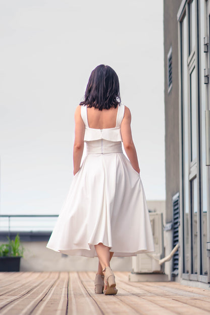 beautiful woman in a white two piece dress with corset top with a ruffle over the breast seam and long flowy skirt. this picture is made from the back, walking away