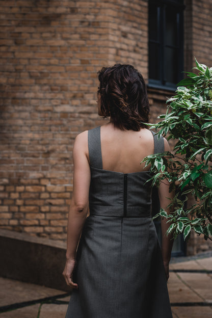 beautiful brunette on the streets in a gray two piece office dress - a corset top and a triangle skirt. thi is a picture from the back and the beautiful top has a high-quality black tractor zipper